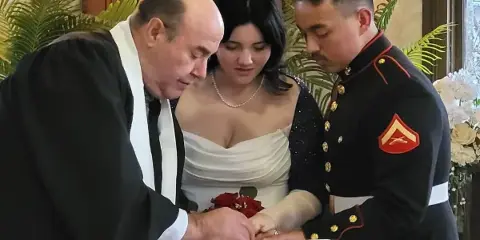 A wedding officiant in clerical robes performing a ring exchange ceremony with a bride and groom.