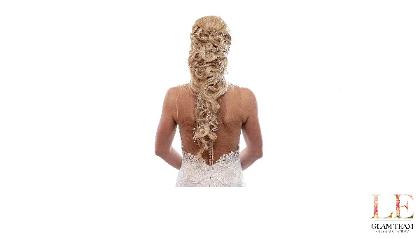 Bride shown from behind wearing an elaborate braided updo with crystal hair accessories and a white lace wedding dress.
