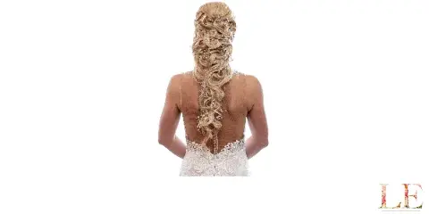 Bride shown from behind wearing an elaborate braided updo with crystal hair accessories and a white lace wedding dress.