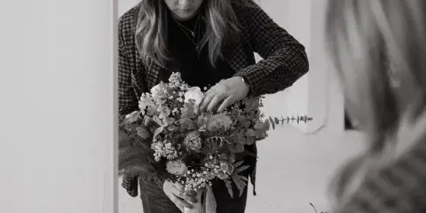 A woman in a plaid shirt arranging a wedding bouquet with roses and greenery.