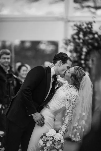 A black and white photograph of a bride and groom kissing during their wedding ceremony.