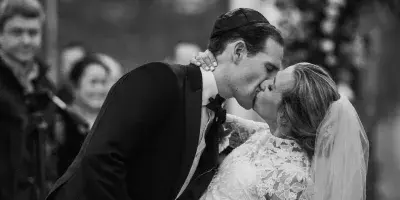 A black and white photograph of a bride and groom kissing during their wedding ceremony.
