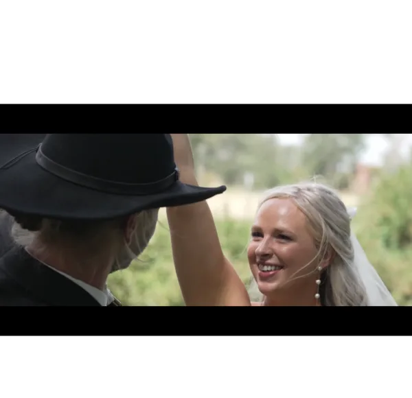 A bride smiling while dancing with her groom in a black cowboy hat during a wedding.