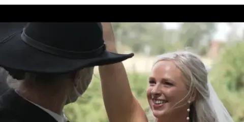 A bride smiling while dancing with her groom in a black cowboy hat during a wedding.