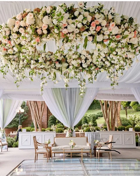 A large, cascading floral arrangement featuring white and pink roses and greenery suspended over a wedding reception area.