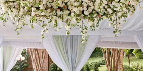 A large, cascading floral arrangement featuring white and pink roses and greenery suspended over a wedding reception area.