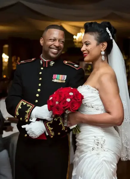 A bride and groom in formal wedding attire standing together in a ballroom.