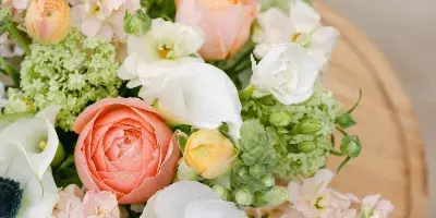 A close-up of a floral arrangement with white anemones, peach roses, and green hydrangeas resting on a wooden surface.