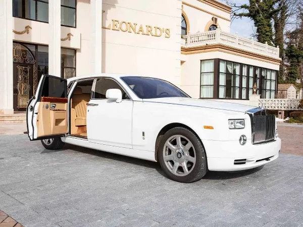 White Rolls-Royce Phantom luxury vehicle parked outside a building with the rear door open, revealing the interior.