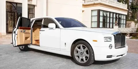 White Rolls-Royce Phantom luxury vehicle parked outside a building with the rear door open, revealing the interior.