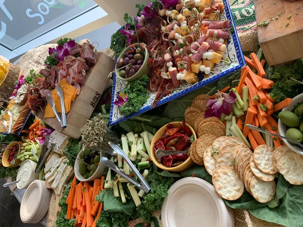 A large catering table filled with a charcuterie board, cheese, crackers, and fresh vegetable sticks.