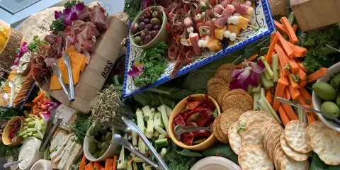 A large catering table filled with a charcuterie board, cheese, crackers, and fresh vegetable sticks.