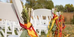 Rows of white folding chairs decorated with floral arrangements and ribbons set up outdoors for a wedding.
