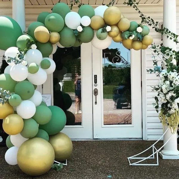 Decorated venue entrance with a green, white, and gold balloon arch and floral arrangements.