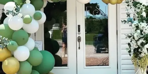 Decorated venue entrance with a green, white, and gold balloon arch and floral arrangements.