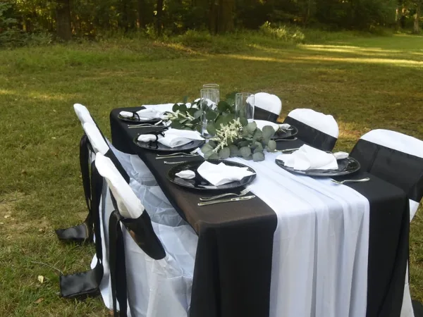A set event table with black and white linens, chairs, and floral centerpieces in an outdoor setting.