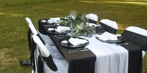 A set event table with black and white linens, chairs, and floral centerpieces in an outdoor setting.