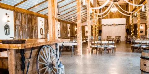 Interior of a rustic barn wedding venue featuring a wooden bar, string lights, and reception tables.