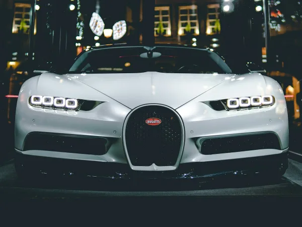 Front view of a white luxury Bugatti sports car with illuminated headlights in a dark setting
