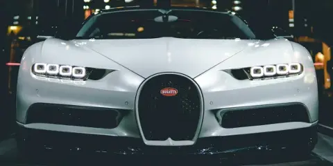 Front view of a white luxury Bugatti sports car with illuminated headlights in a dark setting