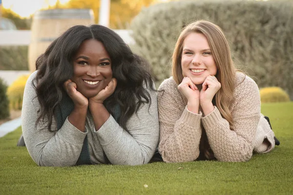 Two smiling women lying on grass in an outdoor portrait setting