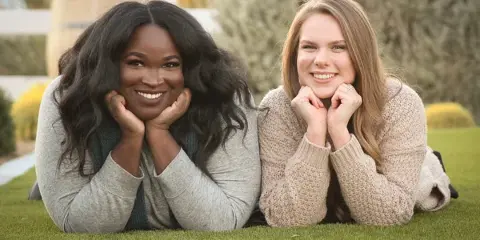 Two smiling women lying on grass in an outdoor portrait setting
