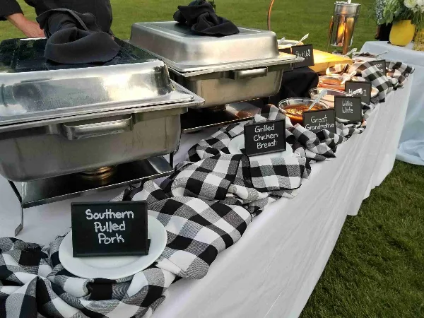 Outdoor catering buffet featuring chafing dishes and labeled barbecue dishes including Southern Pulled Pork and Grilled Chicken Breast.