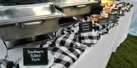 Outdoor catering buffet featuring chafing dishes and labeled barbecue dishes including Southern Pulled Pork and Grilled Chicken Breast.