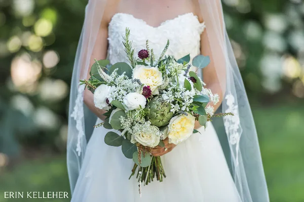 Bride in a white lace gown holding a custom bouquet of white and yellow roses, eucalyptus, and greenery.