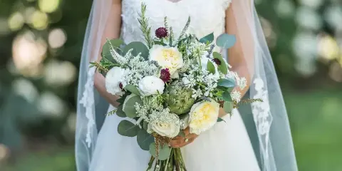 Bride in a white lace gown holding a custom bouquet of white and yellow roses, eucalyptus, and greenery.