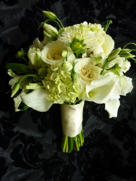 A white wedding bouquet with roses, calla lilies, and hydrangeas wrapped in a cream ribbon.
