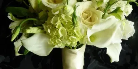 A white wedding bouquet with roses, calla lilies, and hydrangeas wrapped in a cream ribbon.