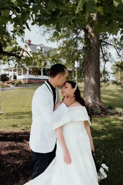 A bride and groom embracing on the lawn in front of a historic white mansion.