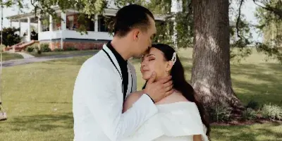 A bride and groom embracing on the lawn in front of a historic white mansion.