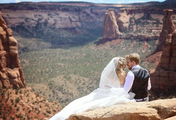 A bride and groom embracing on a rocky cliff overlooking a vast canyon landscape.