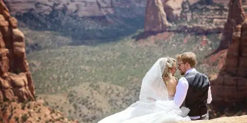 A bride and groom embracing on a rocky cliff overlooking a vast canyon landscape.