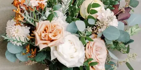 A close-up of a wedding bouquet featuring peach and white roses, eucalyptus leaves, and dried grasses tied with a ribbon.