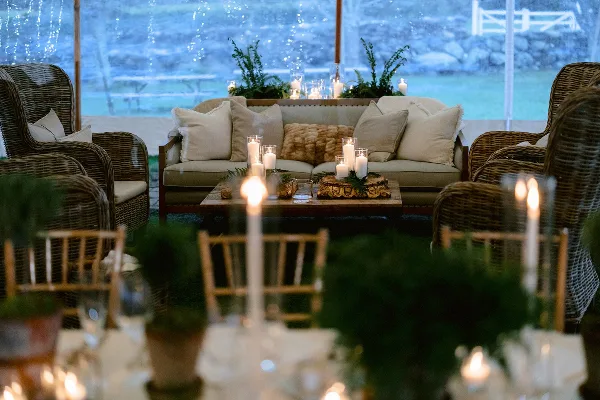 A professionally decorated event lounge area featuring a sofa, wicker chairs, and a table with candles and greenery.