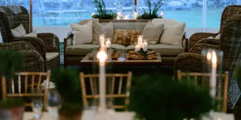 A professionally decorated event lounge area featuring a sofa, wicker chairs, and a table with candles and greenery.