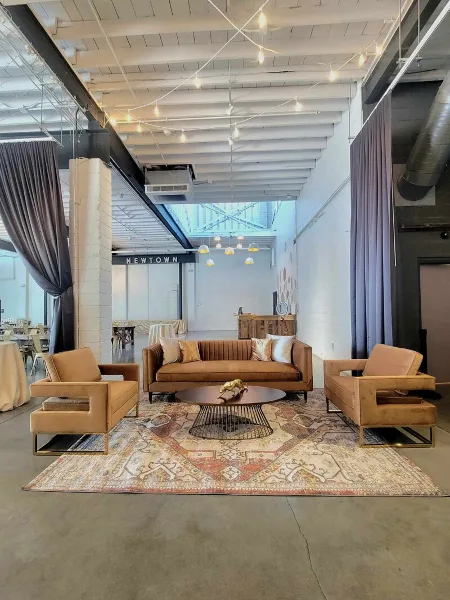 A vintage-style lounge set with a brown sofa, two armchairs, and a patterned rug arranged in a studio space.