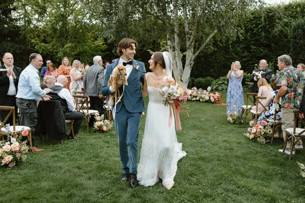 A bride and groom walking down the aisle during an outdoor wedding ceremony with guests seated on either side.