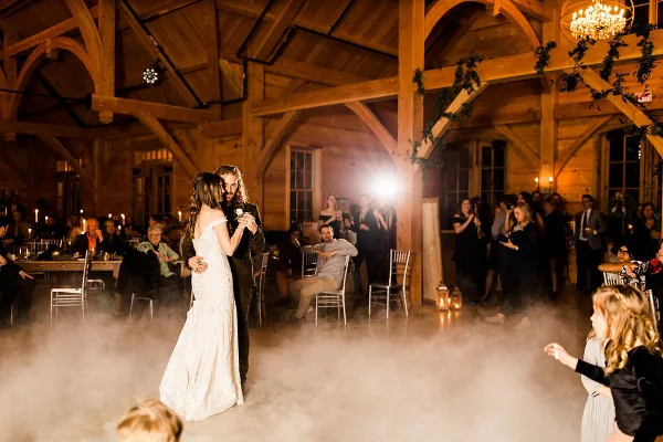 A wedding reception in a wooden barn with set dining tables and a couple dancing.