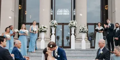 A bride and groom kissing on the steps of the Missouri History Museum while guests throw petals.