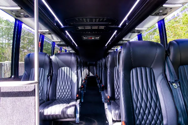Interior view of a shuttle bus with rows of black leather seats and overhead lighting.