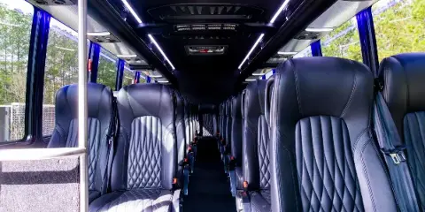 Interior view of a shuttle bus with rows of black leather seats and overhead lighting.