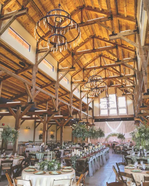 Interior view of a large timber-frame event hall set up for a wedding with round tables and chandeliers.