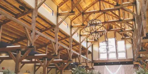 Interior view of a large timber-frame event hall set up for a wedding with round tables and chandeliers.