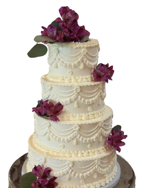 A four-tier white wedding cake decorated with swag-style frosting and purple alstroemeria flowers.