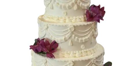 A four-tier white wedding cake decorated with swag-style frosting and purple alstroemeria flowers.