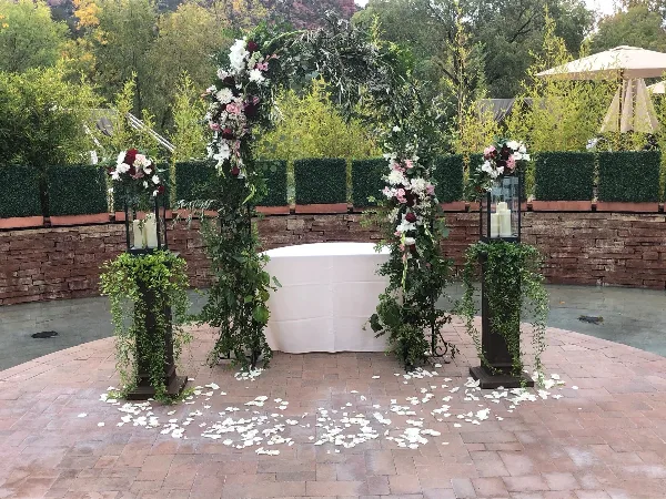 Outdoor wedding ceremony setup featuring a floral arch, white altar table, and pedestals with candles and flowers.